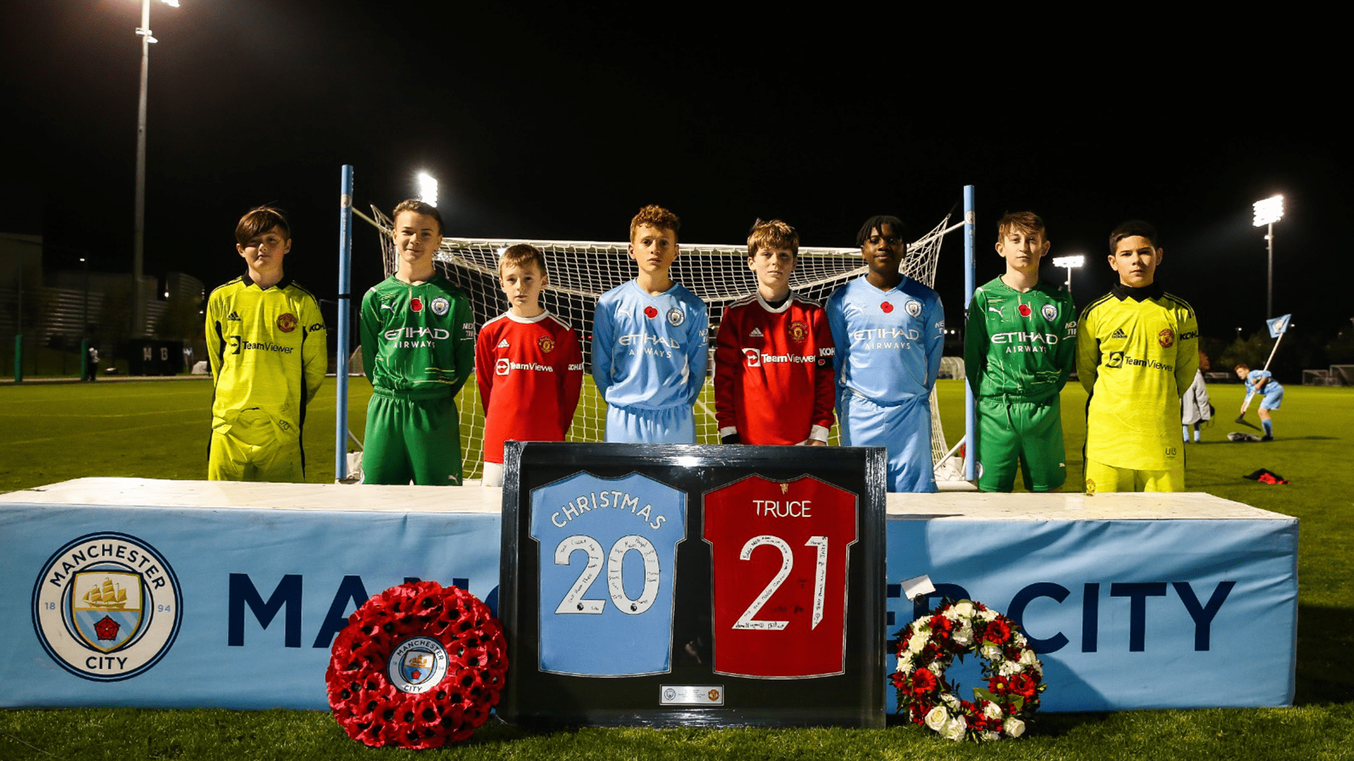 Manchester City and Manchester United Academy players stand together with framed and signed 20 and 21 football shirts marking the year 2021 as part of their special City United / United City truce tournament on 11 November 2021.